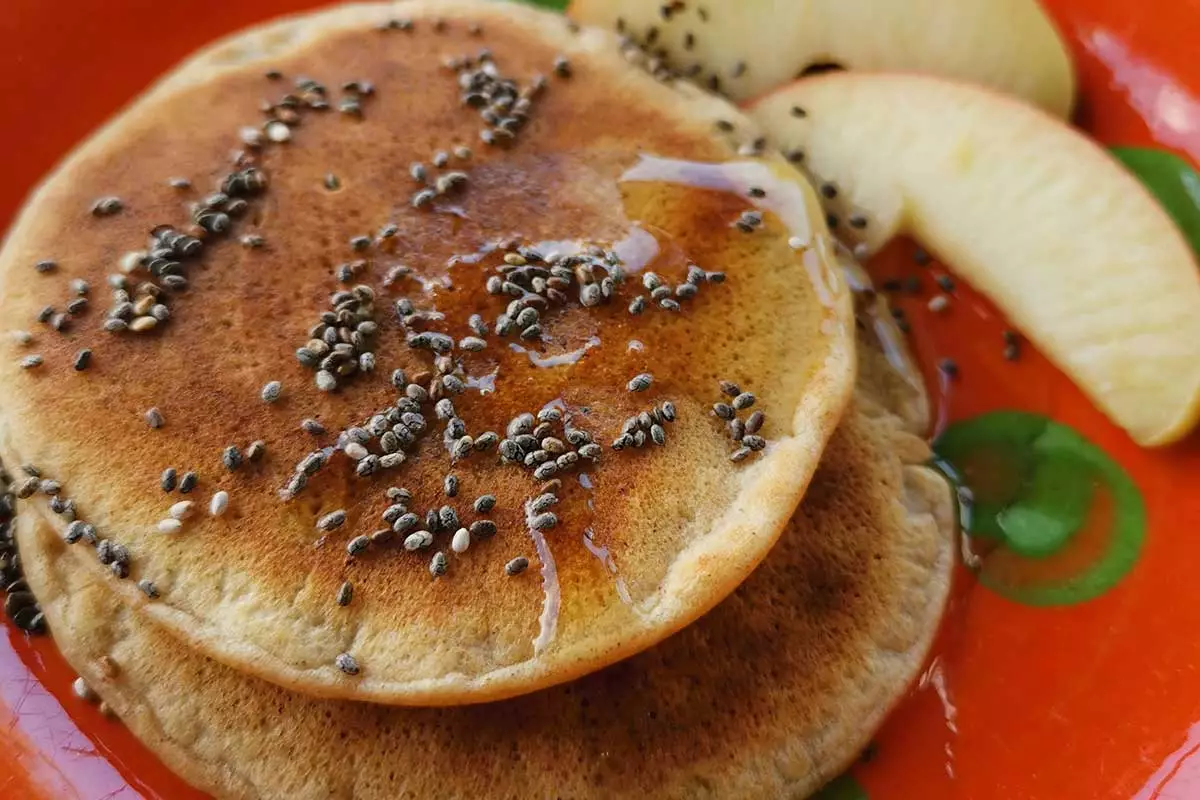 Heerlijke vegan pancakes van De Groene Stadshut liggen op een bord met stukjes appel en chiazaad.
