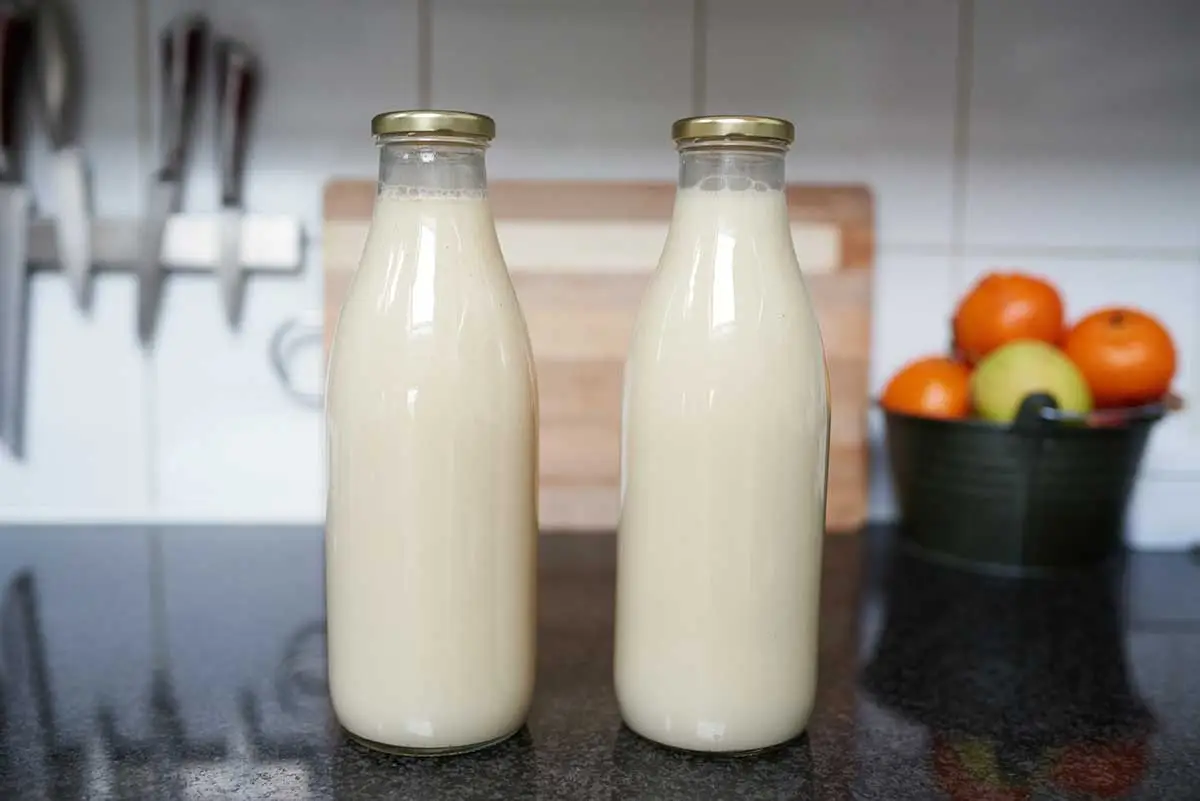 2 volle glazen flessen zelfgemaakte havermelk staan op het aanrecht.