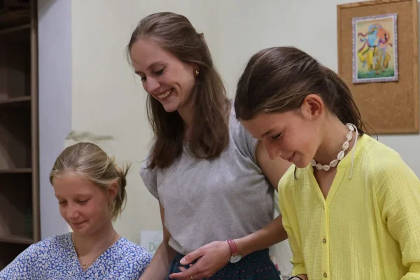 Een jonge vrouw staat tussen 2 meisjes tijdens een leuke workshop. Ze glimlachen.